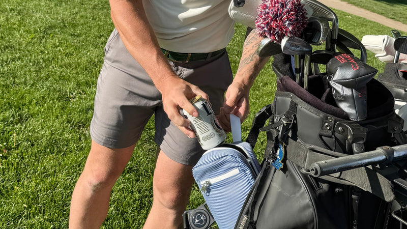 Man preparing to hit a golf ball on a golf course with a golf cart in the background.